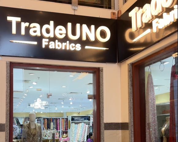 TradeUNO Fabrics storefront with a large illuminated black sign and glass windows showing the interior fabric display.