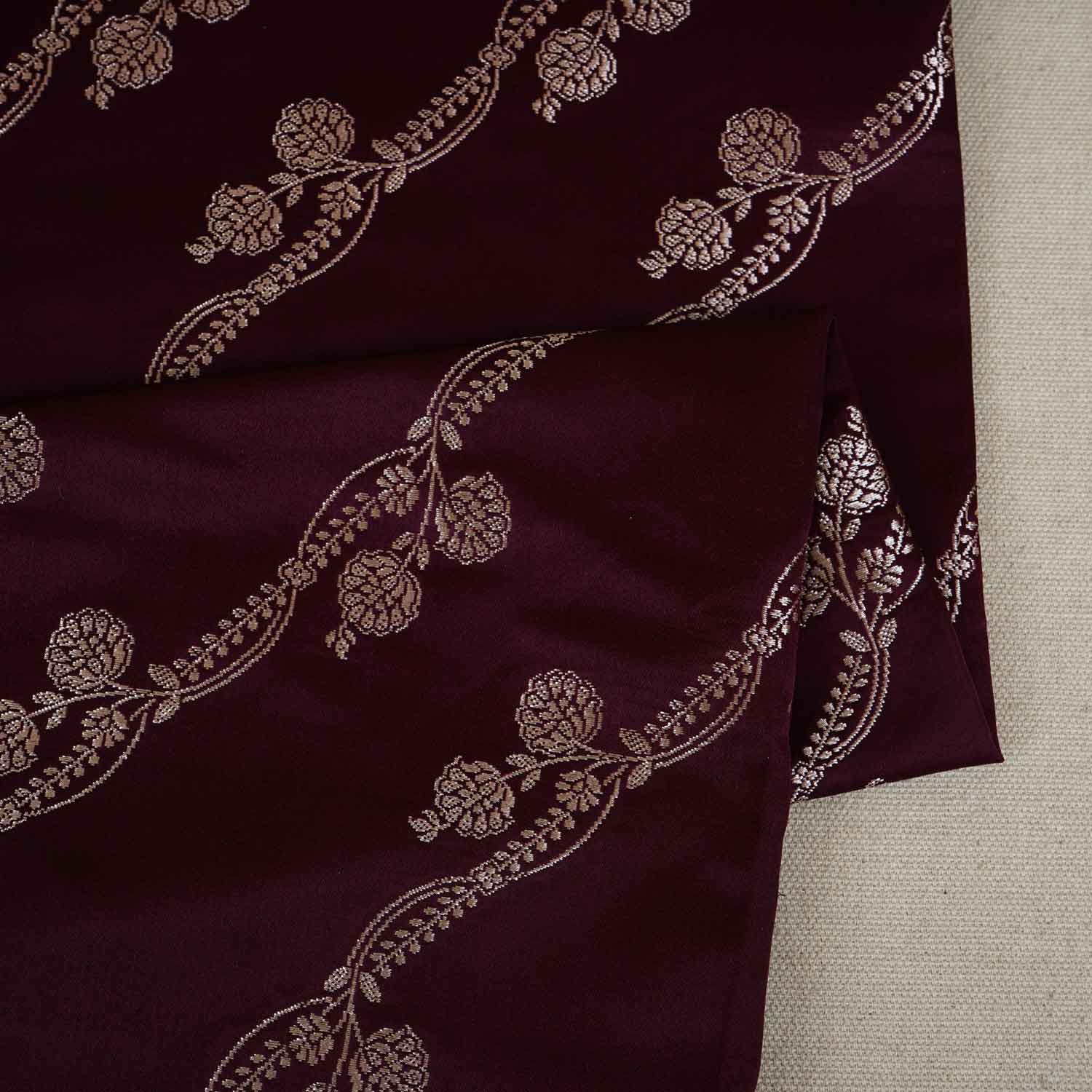 Close-up of dark purple fabric with intricate gold embroidery on a neutral background